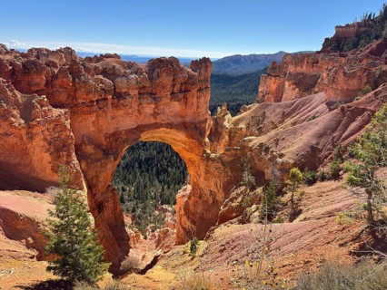 Natural stone arch in an impressive canyon landscape with views of dense forests and steep slopes,