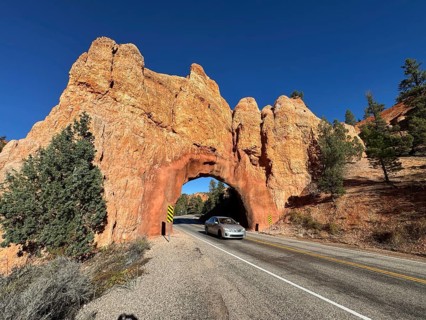 Red sandstone arch over a road in a desert landscape with clear blue skies and a passing car, Bryce
