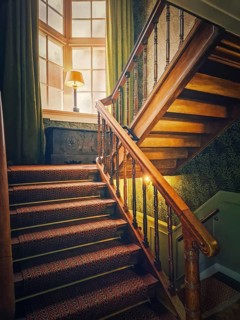 A vintage, wooden staircase with classic balusters leads up to a soft light that filters through