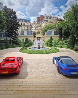 Two luxury sports cars parked in the driveway of an opulent Parisian mansion with view to a