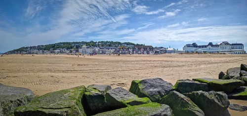 Panoramic view of Trouville-sur-Mer sandy beach, Normandy, France. Large, moss-covered breakwater
