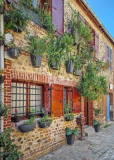 A quaint old masonry building with wooden shutters, adorned with numerous planters overflowing with