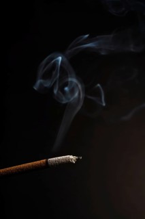 Close-up of a burning incense with white smoke coming out illuminated on a black background