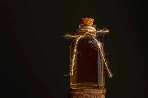 Close-up of a glass bottle with cork stopper and raffia rope with rosemary oil on a dark background