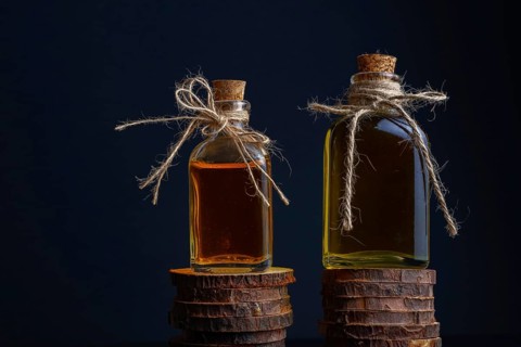 Close-up of two glass bottles with cork stopper and raffia string with rosemary oil and rose oil on