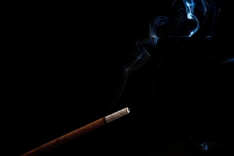 Close-up of a burning incense with white smoke coming out illuminated on a black background