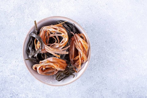 Pasta with carrots and spinach in a round plate on a light textured background, top view, space for