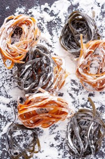 Pasta with carrots and spinach on a floured table, space for text