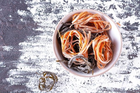 Pasta with carrots and spinach in a round plate on a table covered with flour, top view, space for