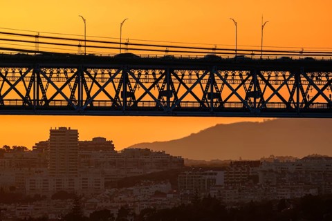 Striking close-up of famous 25 de Abril bridge, its silhouette against bright orange sunset sky.