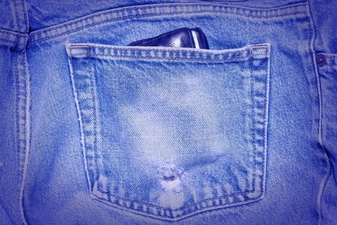 A Worn and tattered blue Jeans pocket. Carrying a wallet in your back pocket can hurt your back
