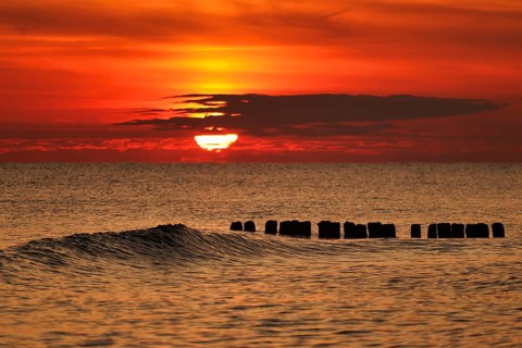 A vivid sunset over the sea with gentle waves and an orange sky creating a tranquil atmosphere.