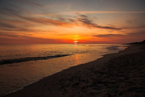 A serene sunset over the sea with golden skies and gentle waves lapping at the sandy beach. Sea