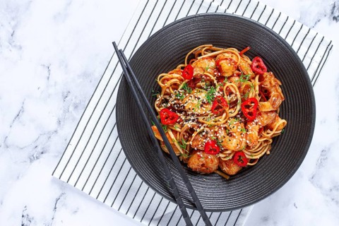 Delicious shrimp stir-fry with noodles and colorful vegetables served in a black bowl on a striped