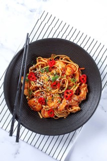 Delicious shrimp stir-fry with noodles and colorful vegetables served in a black bowl on a striped