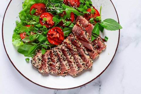 Fried tuna in sesame seeds, sliced on a plate, with fresh salad, on a white plate, homemade
