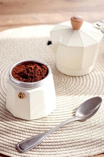 Geyser coffee maker with ground coffee and a spoon on the background of a woven rug, coffee