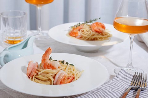 Pasta with shrimp and thyme, served on a white plate, with a glass of white wine, the table is set,