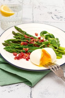 Poached egg with fork, asparagus, bacon slices and herbs, on a white plate, breakfast, close-up, no