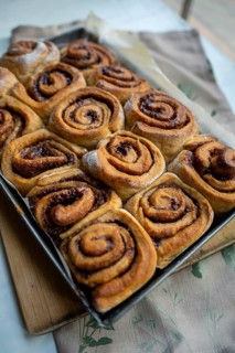 Freshly baked cinnamon roll on a wooden board with a small pot of milk