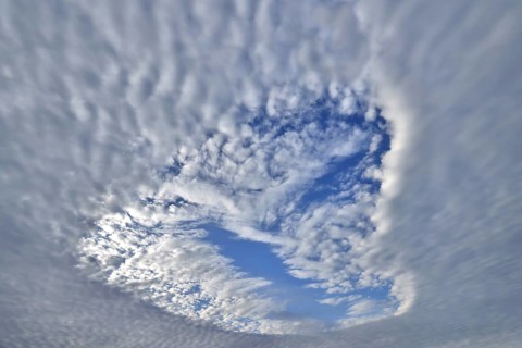 Heart-shaped hole in low-lying closed cloud cover provides a view of the blue sky with sheep