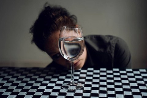Woman's face behind a wine glass, with reflection in water