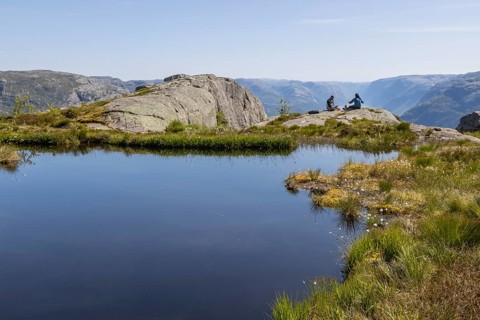 Two people sitting on a rock by a mountain lake, above the Preikestolen hiking trail and high above