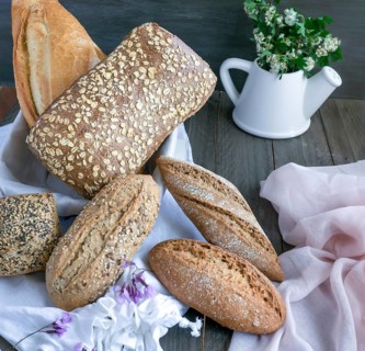 Artisanal bread loaves and rolls featuring various grains and seeds arranged on a white cloth,