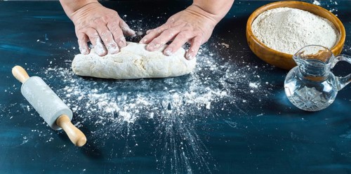 Baker's hands carefully kneading uncooked dough on a dark kitchen counter, preparing traditional