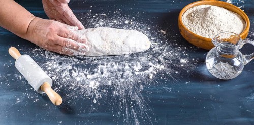 Female hands preparing fresh artisanal bread dough on a dark kitchen table. Baking ingredients