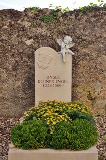 Children's grave with angel figure and beautiful floral decoration on a cemetery wall, Upper