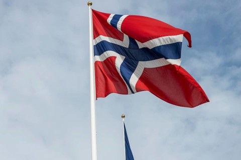 The national flag of Norway fluttering against the blue sky and gentle clouds. Oslo, Østlandet,