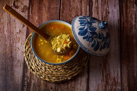White and blue soup tureen with chicken noodle and vegetable soup with a wooden spoon