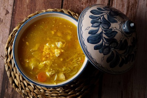 White and blue soup tureen with chicken noodle soup and vegetables with the lid open