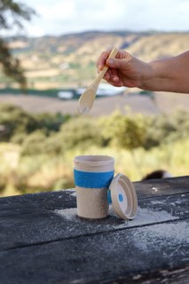 Person's hand adding a white powder with a wooden spoon into a reusable eco-friendly cup, enjoying
