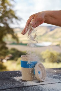 Hand pouring white powder from hand into a reusable portable mug on a wooden table, enjoying