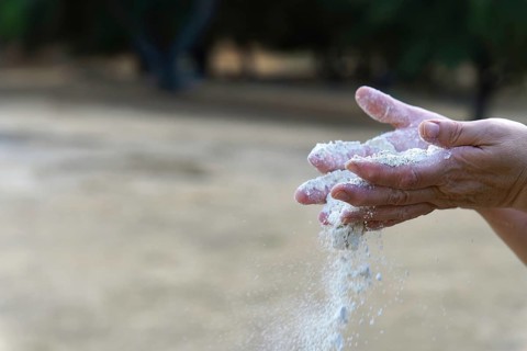 Hands releasing loose sand, grains falling through aged fingers to symbolize time, fragility,
