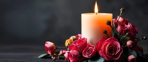 A lit candle surrounded by pink roses against a dark background, creating a romantic and serene