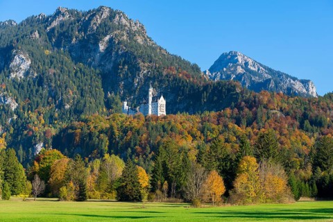Neuschwanstein Castle in an extensive autumn landscape with mountains and green meadows in the