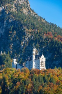 Neuschwanstein Castle high up on an autumn-colored hill in front of imposing mountains, Schwangau,