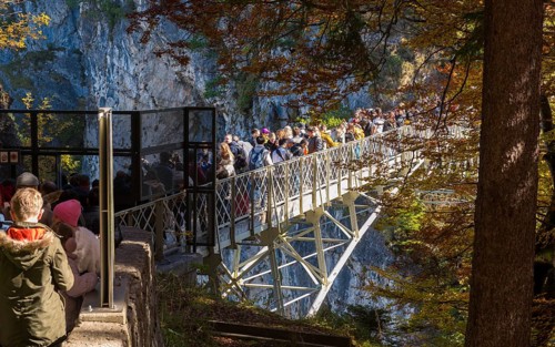 People queue on Marienbrücke near Neuschwanstein Castle, in an autumn forest landscape, Schwangau,