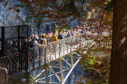 People on the Marienbrücke near Neuschwanstein Castle in autumn, surrounded by trees and rocks,