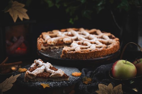 Apple cake with powdered sugar on a dark table with autumn decorations