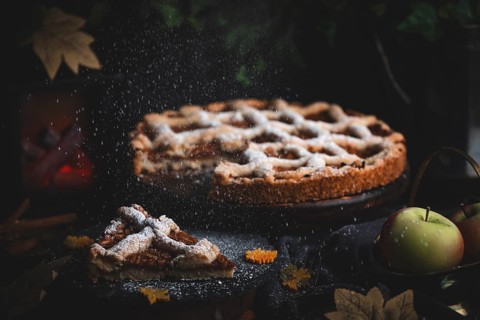 Icing sugar falls on apple pie surrounded by autumn leaves in a dark environment