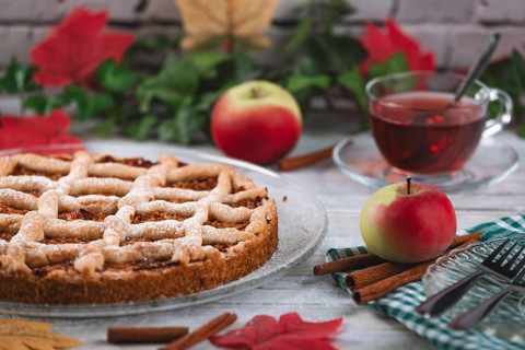 Apple cake with powdered sugar next to tea and apples, surrounded by autumn leaves and cinnamon