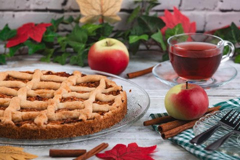 Apple pie with tea and apples surrounded by autumn leaves and cinnamon sticks