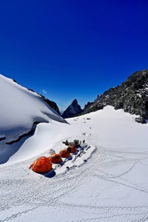 Tents on snowy areas, in the background the l'Aiguille Noire de Peuterey mountain, Pointe