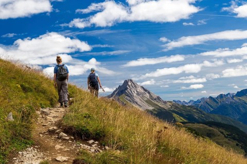Two hikers on a trail in mountainous landscape under blue sky, Schröcken, Austria