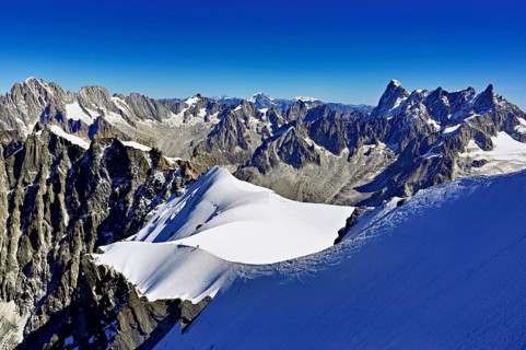 Mountaineers climb over a snow-covered ridge with Grandes Jorasses mountain in the background,