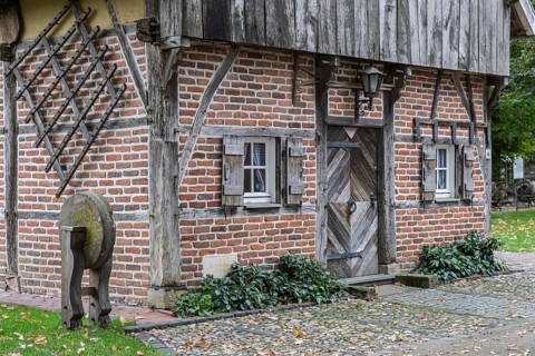 Small half-timbered house with wooden door, whetstone and cobblestones, framed by ivy and leaves,
